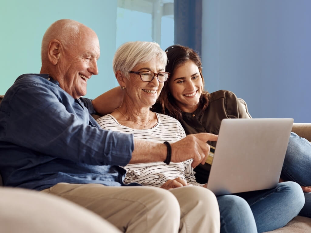 Smiling older couple and a younger family member reviewing questions to ask before choosing a home care agency on a laptop