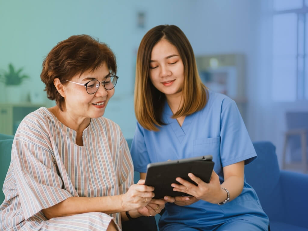 Senior woman and caregiver in blue scrubs reviewing a tablet together during an in-home care visit.