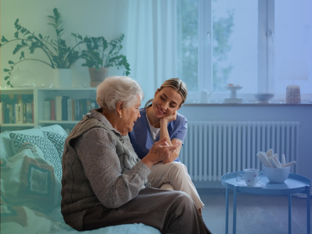 Smiling caregiver listening to an older woman during dementia care at home in a bright living room