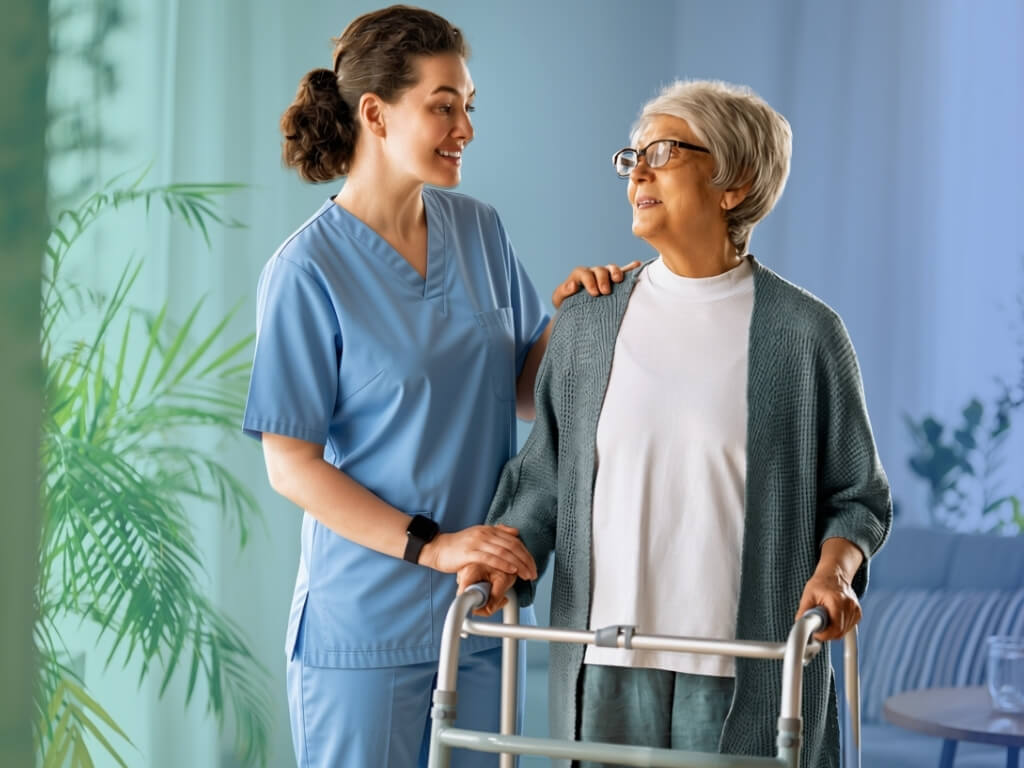Smiling caregiver supporting an older woman using a walker at home as part of mobility assistance