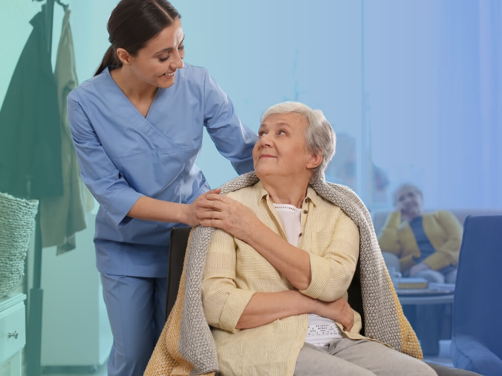 Smiling caregiver resting a hand on a senior woman’s shoulder, providing non-medical home care in a comfortable home setting