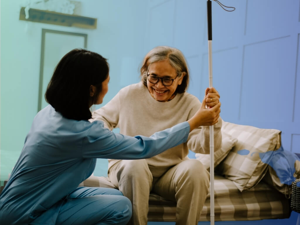Smiling caregiver helping an older woman steady herself with a cane, illustrating safe, supportive incontinence care at home