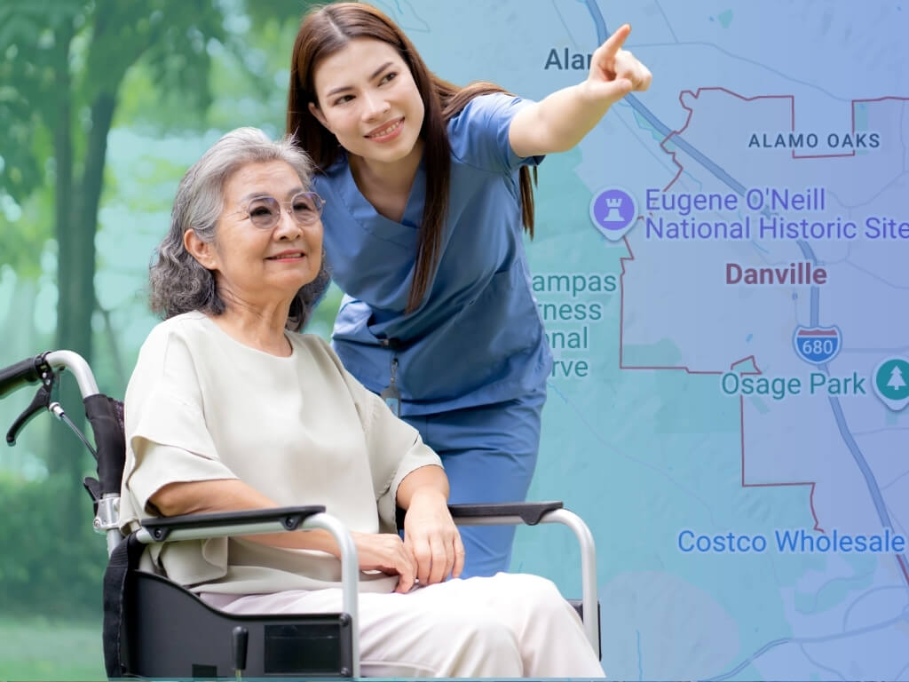 Caregiver beside a smiling senior in a wheelchair, pointing toward a Danville, CA map, showing in-home care in Danville